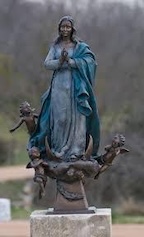 Bronze statue of Our Lady of the Rosary in prayer, attended by cherubs, on the cemetery grounds